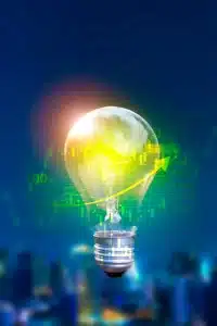 A glowing lightbulb filled with digital financial graphs and arrows, symbolizing ideas and innovation in finance. The background is a blurred cityscape at night, creating a fusion of technology and urban life.