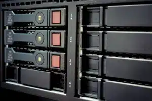 Close-up view of a server rack showing several hard drives installed in numbered slots. Three drives on the left are occupied, with indicator lights visible, while several slots on the right are empty, emphasizing the importance of regular server maintenance for optimal website hosting performance.