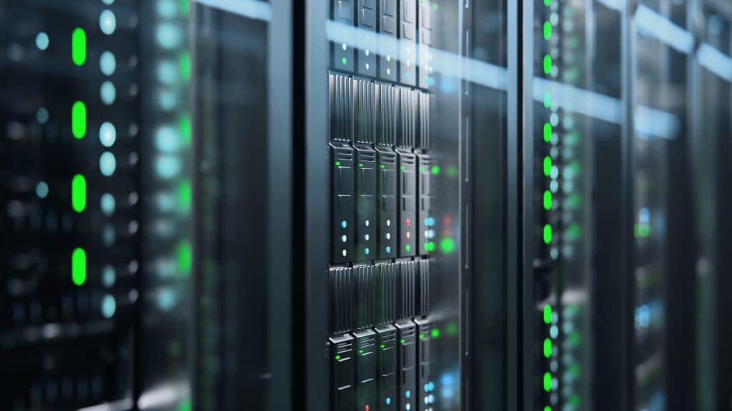 A close-up view of a row of illuminated server racks in a data center, vital for website solutions. The servers display various colored lights, mainly green and blue, indicating activity and status. The perspective is angled and slightly blurred, capturing the essential tech heartbeat for small businesses.