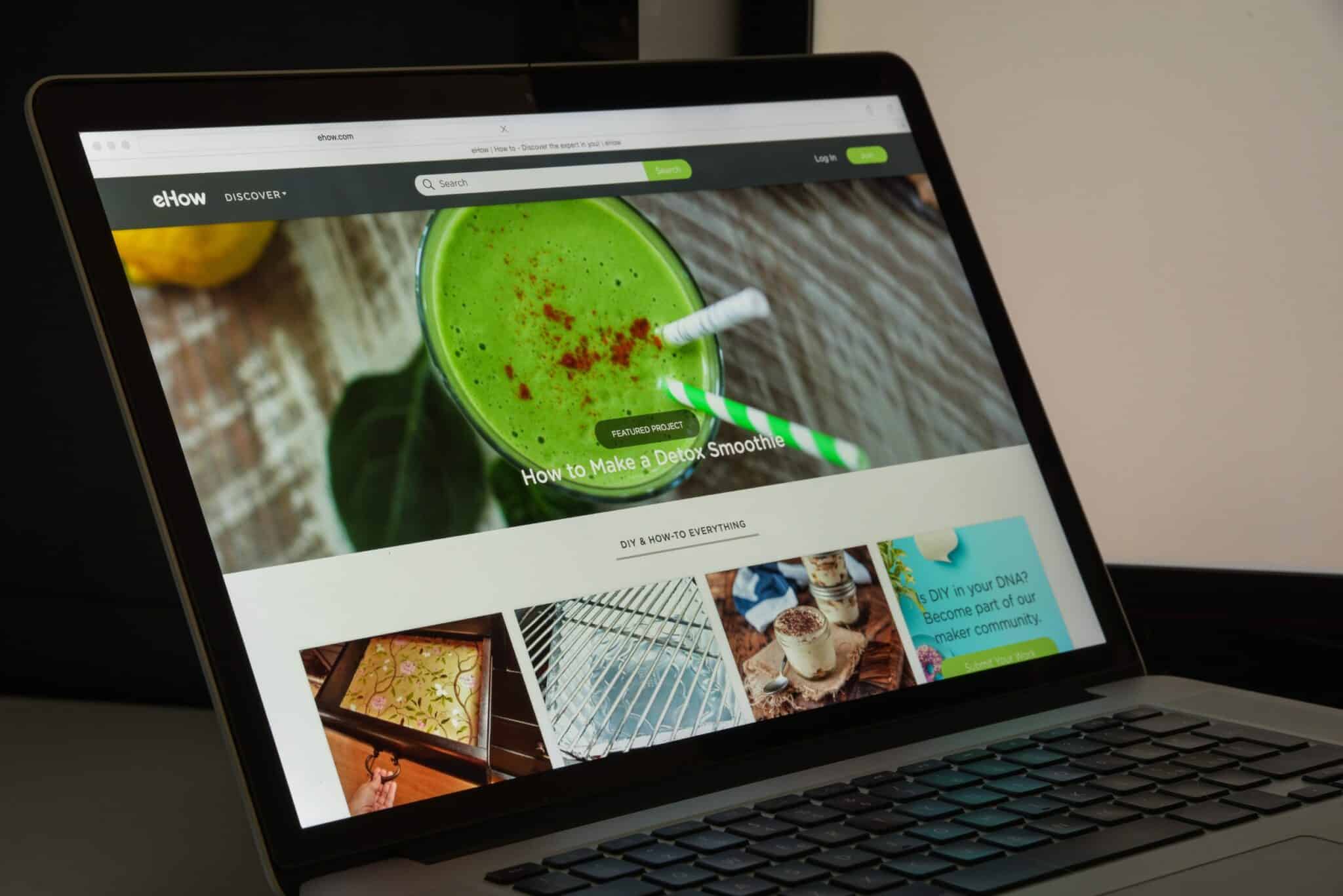 A laptop showcasing the eHow website features an article on crafting a detox smoothie. The screen highlights a green smoothie image with two straws amidst sections on DIY projects. Visible are the keyboard and part of the casing, effortlessly blending draft concepts into a vibrant reality.