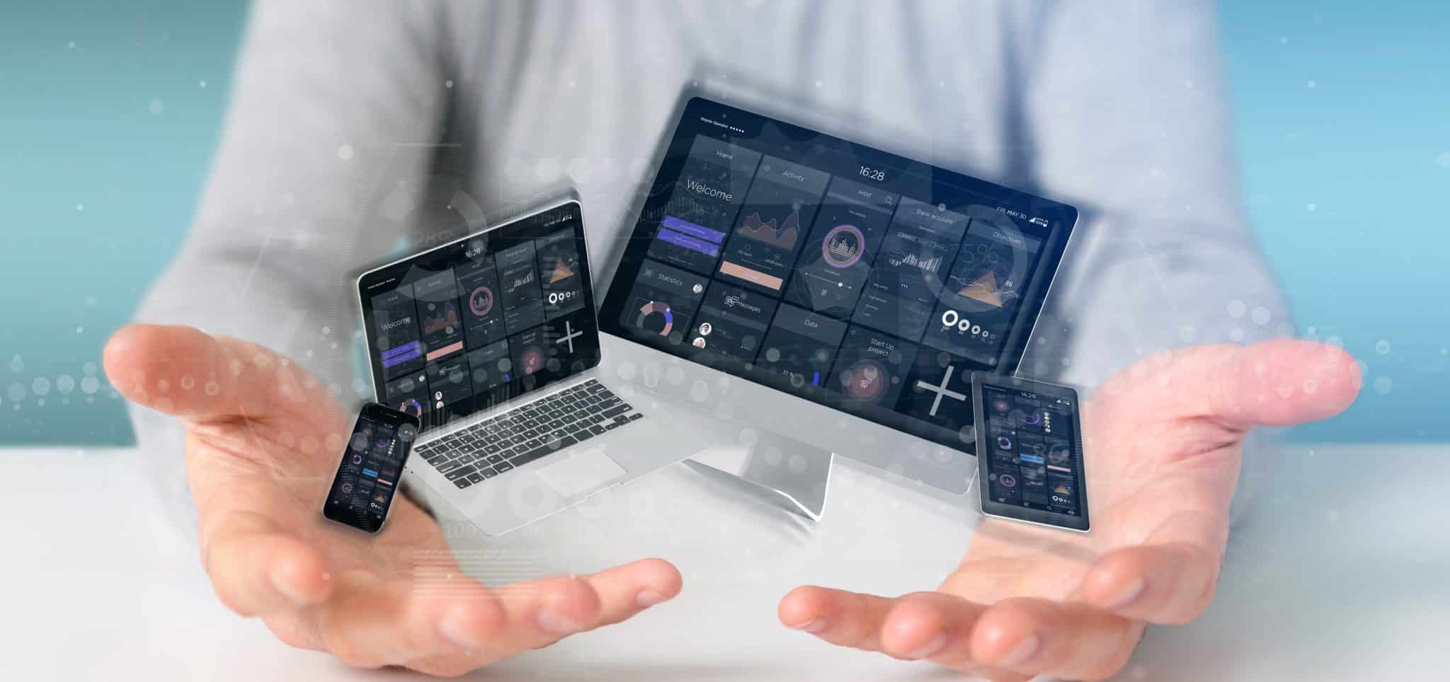 In a futuristic scene set in 2025, a person holds holographic images of a smartphone, laptop, and tablet displaying data dashboards. The blurred background emphasizes these floating tech devices, highlighting an advanced user experience.