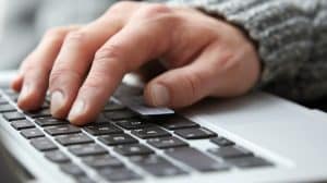 Close-up of a person's hand typing on a laptop keyboard, helping pave the way to website accessibility by 2025. The fingers press the keys with determination, clad in a gray knitted sweater. The laptop boasts a sleek brushed metal finish.