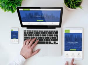 A person uses a laptop, tablet, and smartphone displaying the same modern Responsive Web Design homepage on a white desk, with green plants nearby—showcasing how businesses in 2025 stay connected across all devices.