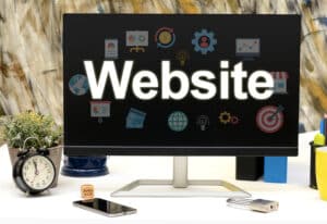 A computer monitor displays the word "Website" with technology and internet-themed icons, reflecting a strong online presence. On the desk are a clock, plant, smartphone, notepad, and a lock, against a blurred background.