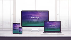 A computer monitor, laptop, tablet, and smartphone sit on a desk, each displaying the same web design homepage with a purple and green gradient background and the text "Web Design." A large window is in the background.
