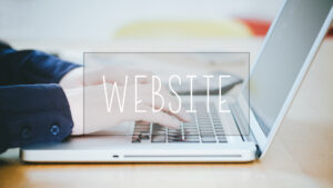 A person types on a laptop keyboard at a desk, with the word "WEBSITE" displayed in large, transparent letters across the image.