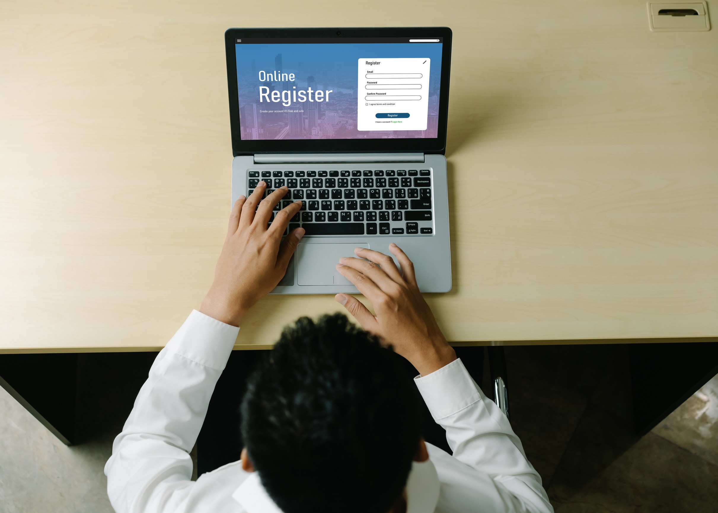 A person in a white shirt uses a laptop on a wooden desk, filling out an online registration form on a high-performing website designed to support local brands.